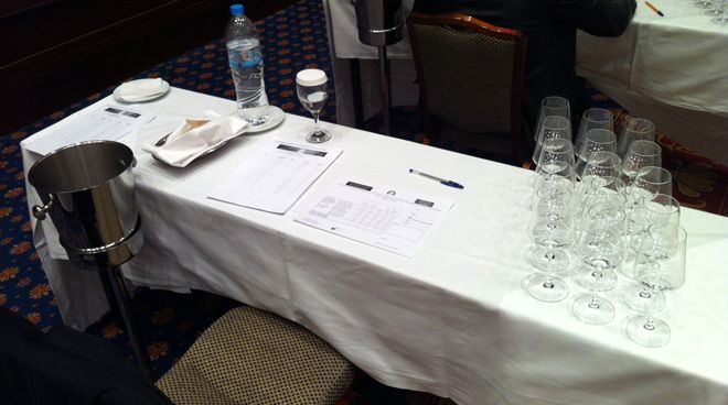A mesa individual de trabalho de cada juiz: Cuspideira, água, pães, fichas de degustação, taças